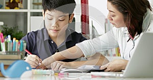 Cute asian mother helping your son doing your homework at home with smile face together.