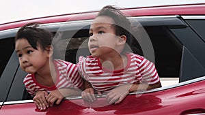 Cute Asian siblings girls smiling and having fun traveling by car and looking out of the car window. Happy family enjoying road tr