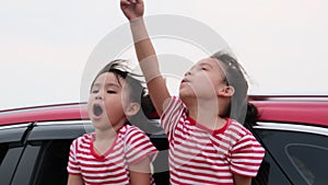 Cute Asian siblings girls smiling and having fun traveling by car and looking out of the car window. Happy family enjoying road tr