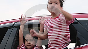 Cute Asian siblings girls smiling and having fun traveling by car and looking out of the car window. Happy family enjoying road tr