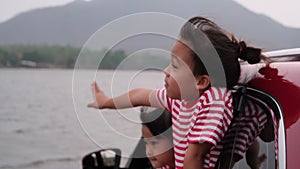 Cute Asian siblings girls smiling and having fun traveling by car and looking out of the car window. Happy family enjoying road tr