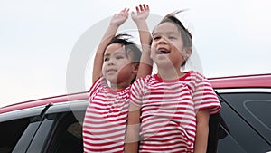 Cute Asian siblings girls smiling and having fun traveling by car and looking out of the car window. Happy family enjoying road tr