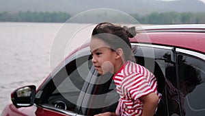 Cute Asian siblings girls smiling and having fun traveling by car and looking out of the car window. Happy family enjoying road tr