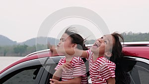 Cute Asian siblings girls smiling and having fun traveling by car and looking out of the car window. Happy family enjoying road tr