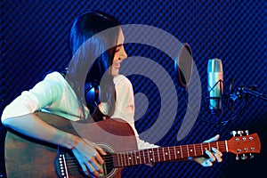 A cute Asian singer and musician playing guitar and sing a song for recording in voice studio