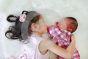 Cute Asian sister embracing sleeping newborn baby lying on white fur background