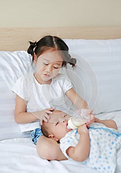 Cute Asian sister feeding milk from bottle for her brother and lying on the bed