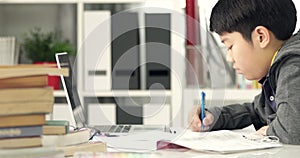 Cute asian teen boy doing your homework with laptop computer at home.