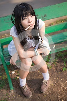 A cute Asian Thai girl is sitting on the bench with a stick in h