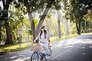 Cute Asian Thai girl in vintage clothing is riding a bicycle in the sunny summer park