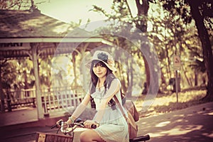 Cute Asian Thai girl in vintage clothing is riding a bicycle, in the sunny summer park.