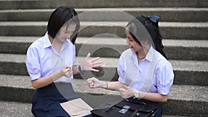 Cute Asian Thai high schoolgirls student couple in school uniform are having fun playing `rock-paper-scissors` with her student fr