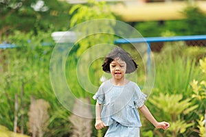 Cute Asian Thai kid girl with short hair, 4 to 6 years old, elementary school age. She is running around in the garden happily and