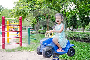Cute asian Thai little girl sitting on the toy car in play ground