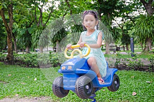 Cute asian Thai little girl sitting on the toy car in play ground