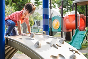 Cute Asian toddler child having fun trying to climb on artificial boulders at playground, Little boy climbing up a rock wall, Hand