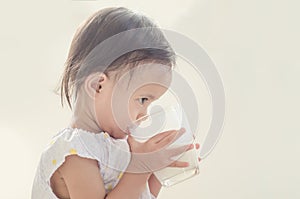 Cute asian toddler girl drinking milk from big glass on white ba