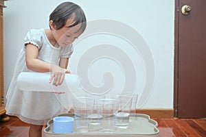 Cute Asian toddler girl having fun playing with water table at home, Wet Pouring Montessori Preschool Practical Life Activities,