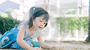 Cute Asian toddler girl playing in sand on outdoor playground