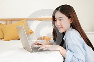 Cute asian woman using computer laptop to work from home in bedroom with breakfast meal in morning.