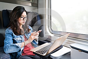 Cute Asian woman using smartphone and laptop on train, copy space on window, business travel or technology concept