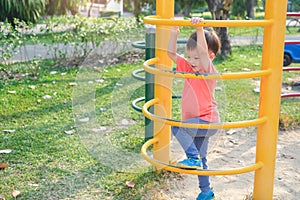 Cute Asian 3 years old toddler baby boy child having fun trying to climb on climbing frame at outdoor playground