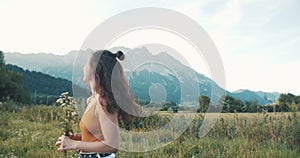 Cute Asian young woman with field flowers on mountain top above sea. Summer nature landscape. Girl tourist standing on