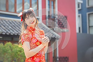 Cute Asian young woman in red cheongsam dress in Chinese new year theme stands smiling happily looking at the camera mong old city