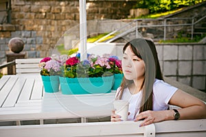 Cute asian young woman in summer cafe outdoors. girl In white T-shirt, with long hair in simple light cozy interior of restaurant
