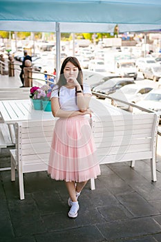 Cute asian young woman in summer cafe outdoors. girl In white T-shirt, with long hair in simple light cozy interior of restaurant