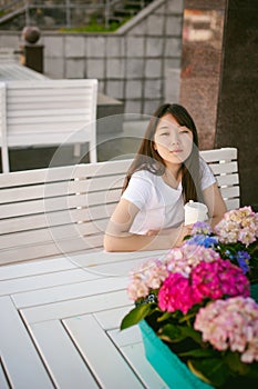 Cute asian young woman in summer cafe outdoors. girl In white T-shirt, with long hair in simple light cozy interior of restaurant