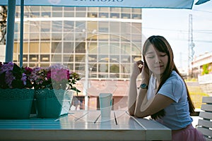 Cute asian young woman in summer cafe outdoors. girl In white T-shirt, with long hair in simple light cozy interior of restaurant