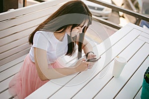 Cute asian young woman in summer cafe outdoors. girl In white T-shirt, with long hair in simple light cozy interior of restaurant