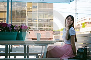 Cute asian young woman in summer cafe outdoors. girl In white T-shirt, with long hair in simple light cozy interior of restaurant