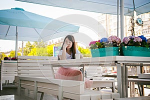 Cute asian young woman in summer cafe outdoors. girl In white T-shirt, with long hair in simple light cozy interior of restaurant