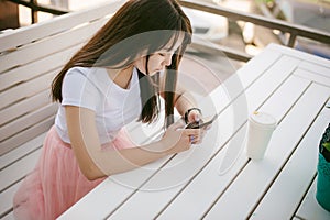 Cute asian young woman in summer cafe outdoors. girl In white T-shirt, with long hair in simple light cozy interior of restaurant