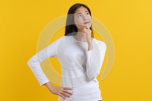 Cute asian young woman in white casual dress looking up and thinking / imagination isolated on yellow background in studio