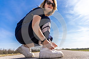 cute athlete woman tying her shoes during a workout on a country road