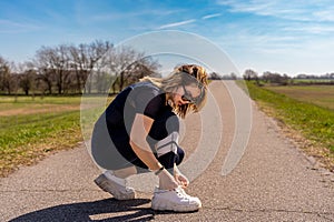 cute athlete woman tying her shoes during a workout on a country road