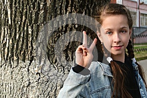 Cute attractive young girl shows her fingers the victory sign  v  background of the bark of large tree.