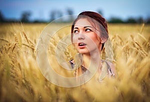 Cute attractive young girl on wheat field during sunset. Pensive look. Romantic atmosphere