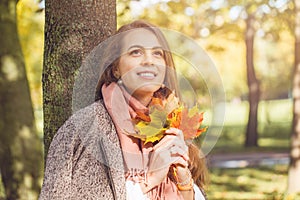 Cute autumn woman holding yellow maple leaf outdoors. Romantic girl in fall park
