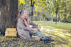 Cute autumn woman sitting near tree outdoors. Romantic girl in fall park