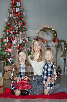 Cute awesome blond mother mom with two girls daughters celebrating New Year Christmas close to xmas tree full of toys in stylish d