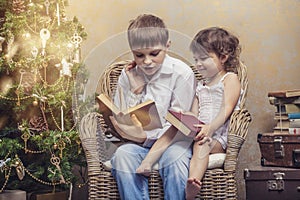 Cute babies boy and girl in a chair reading a book in a interior