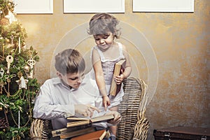 Cute babies boy and girl in a chair reading a book in a interior