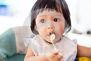 Cute baby asian child girl eating healthy food by herself