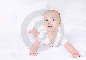 Cute baby with beautiful brown eyes lying in white bed
