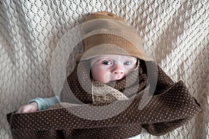 Cute baby with big blue eyes wearing a hat and a huge knitted scarf