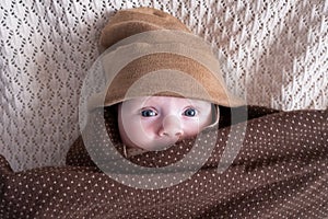 Cute baby with big blue eyes wearing a hat and a huge knitted scarf